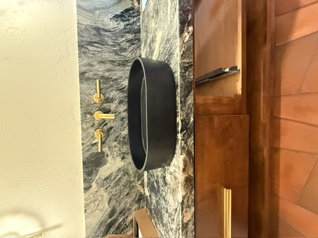 Luxury black vessel sink with gold wall-mount faucet on a natural stone vanity