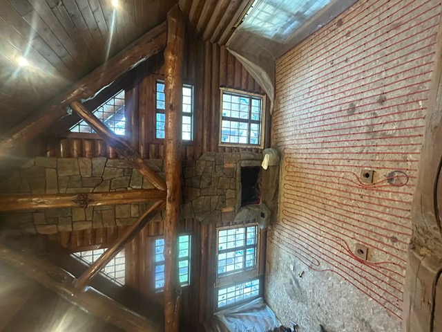 Radiant floor heat installation inside a Montana log home with a stone fireplace